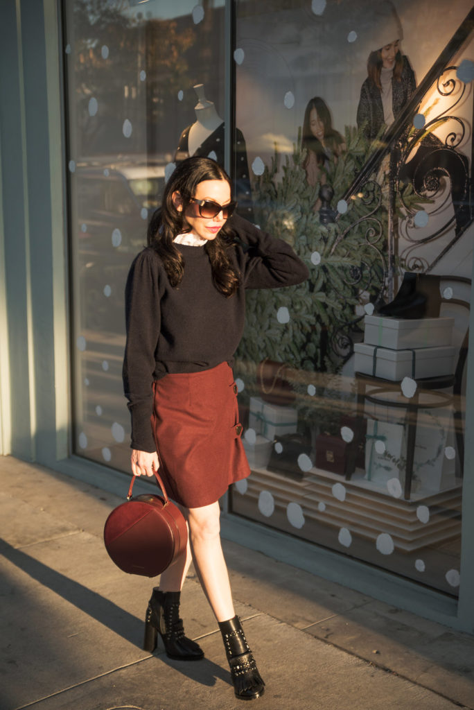 How to Dress Like a Parisian Girl, styling tips featured by top LA fashion blog, Pretty Little Shoppers: image of a woman wearing a Sandro sweater, Storets mini skirt, Tammy & Benjamin bag, Tommy Hilfiger ankle boots, and Oliver Peoples sunglasses.